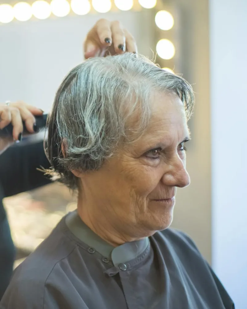 Coiffeuse s'occupant d'une cliente installée sous la cape dans l'espace privatif